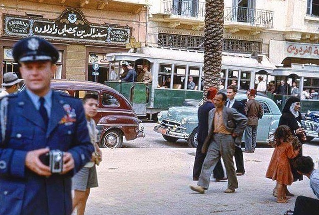 مشهد بيروتي ملوّن عام ١٩٧٠ يضم الترام والسيارات القديمة والمارة